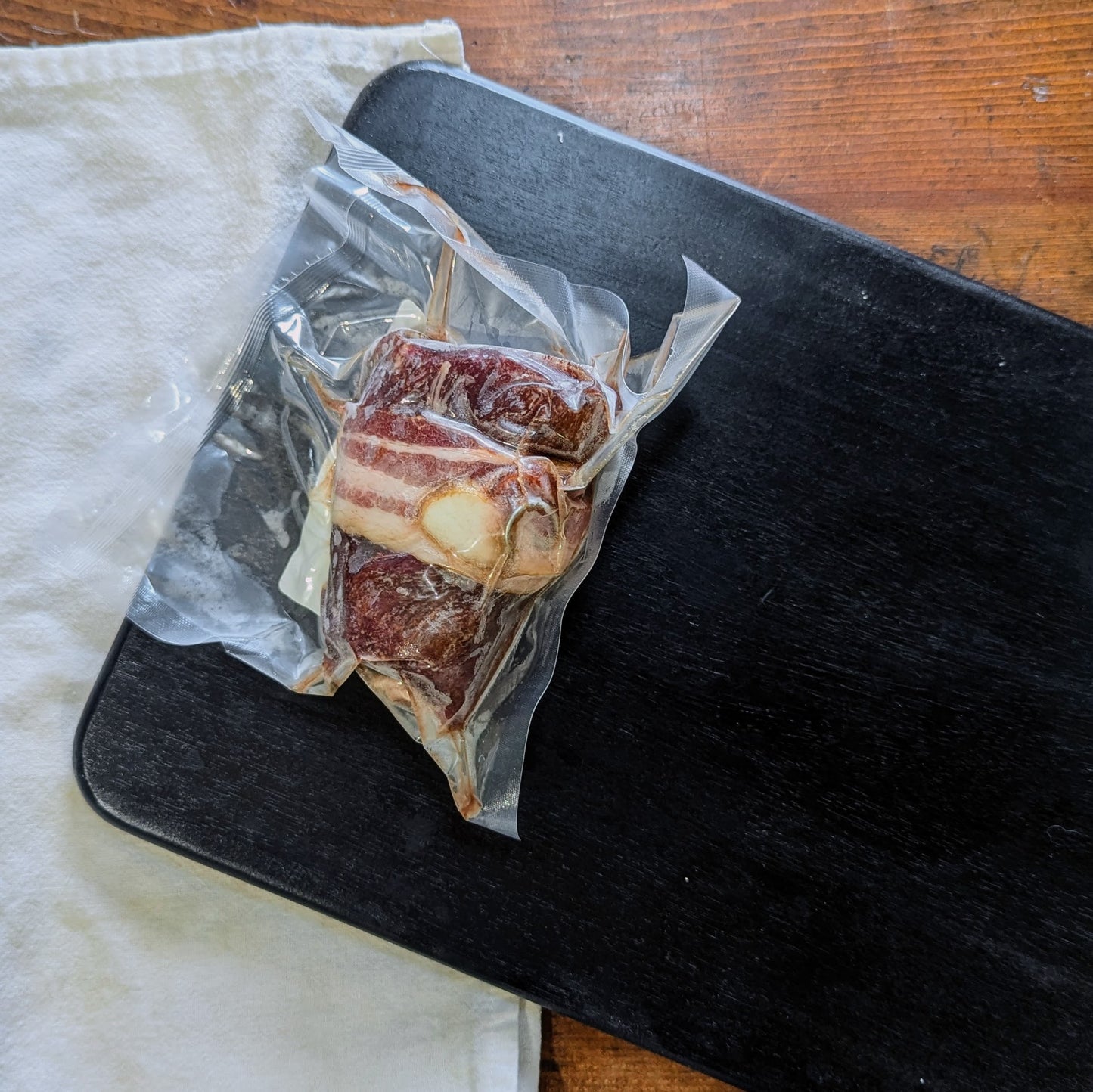 Bacon-wrapped meat on a black cutting board with a white cloth underneath