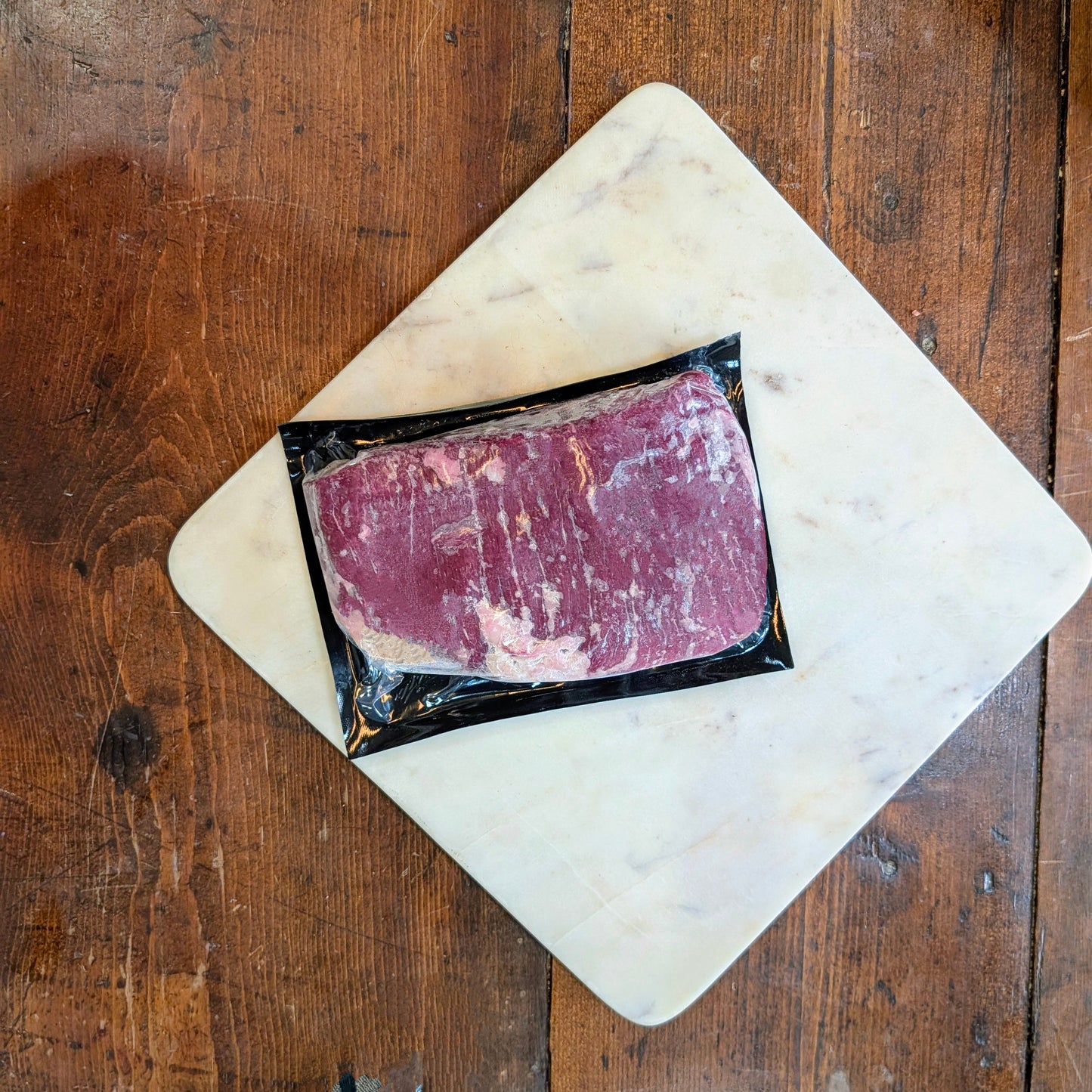 Packaged raw meat on a marble cutting board over a wooden surface