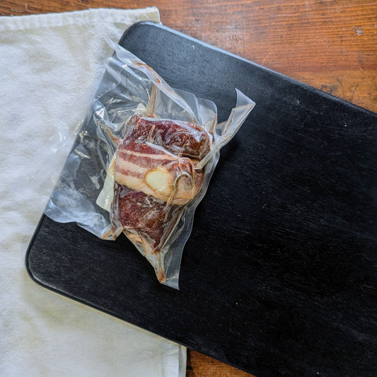 Bacon-wrapped meat on a black cutting board with a white cloth underneath