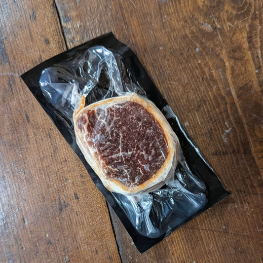 Raw steak on a black plastic tray with clear wrap on a wooden surface