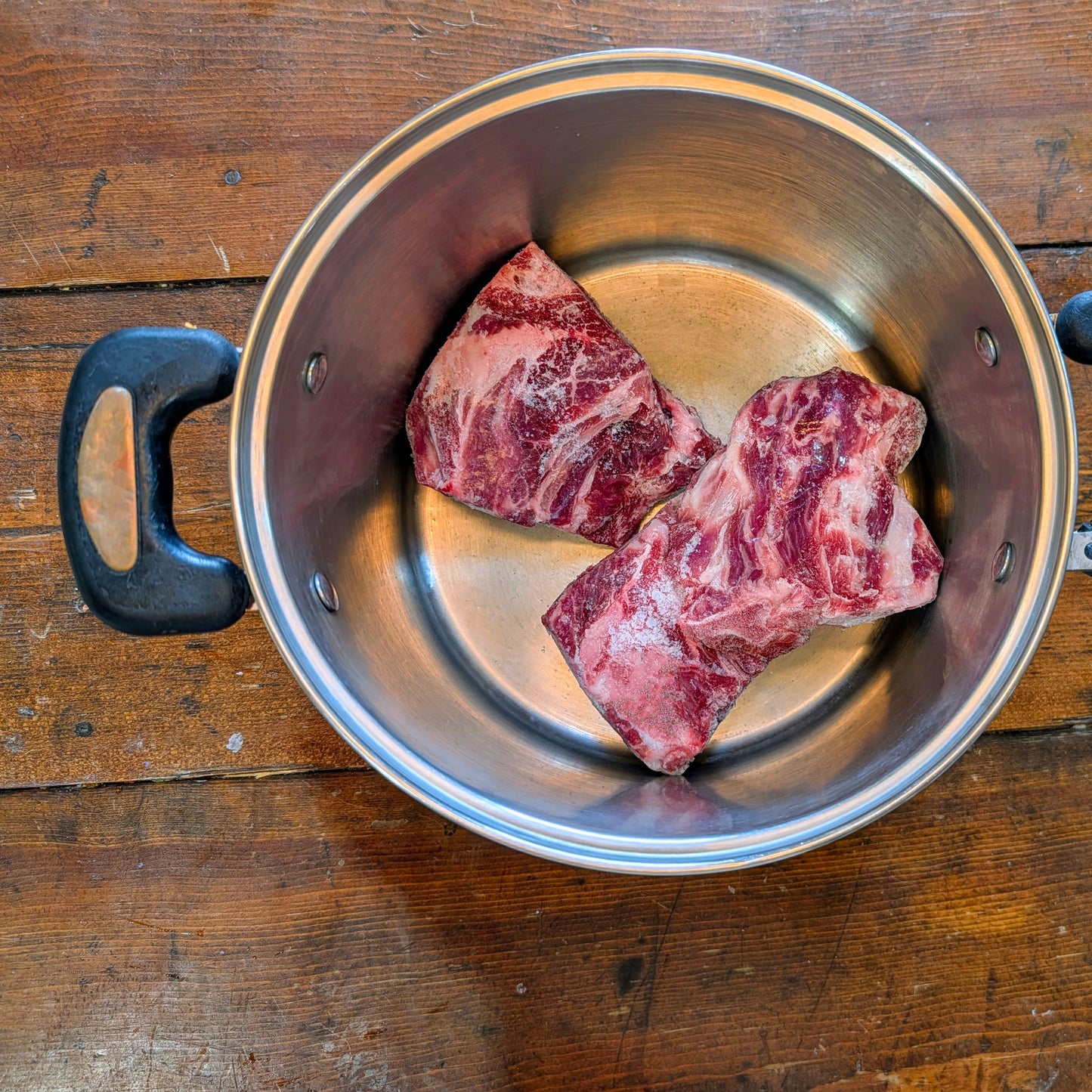 Raw beef pieces in a metal pot on a wooden surface